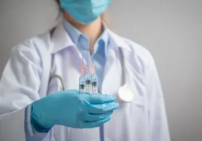 A healthcare worker holds up three syringes with clear medicine